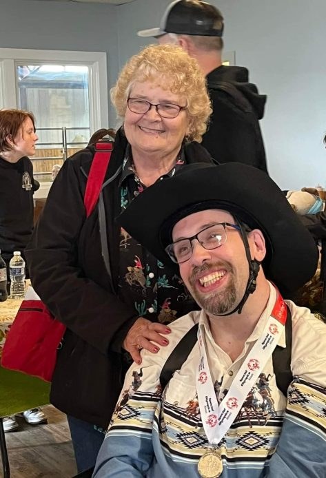 Beth Watter smiling beside her son Nik, who wears a cowboy hat and a medal
